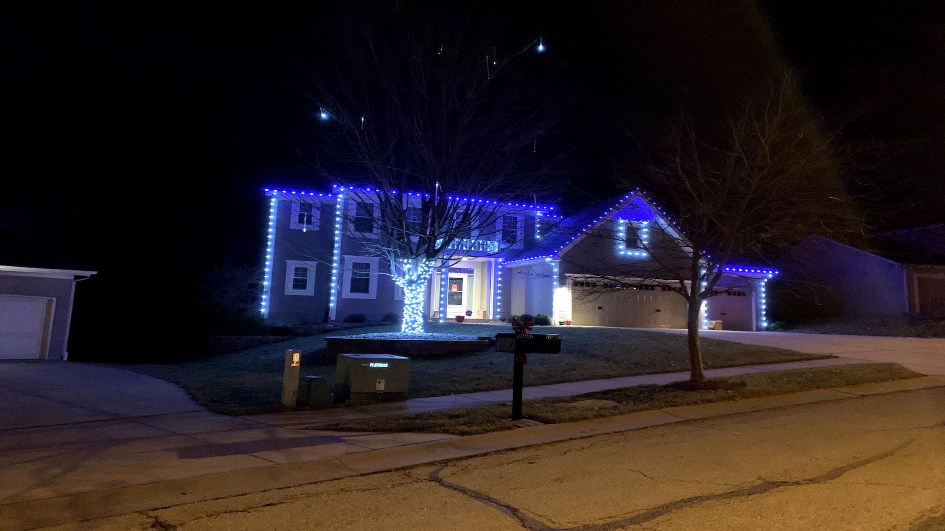 Colonial home with blue Christmas lights and wrapped tree in Kansas City