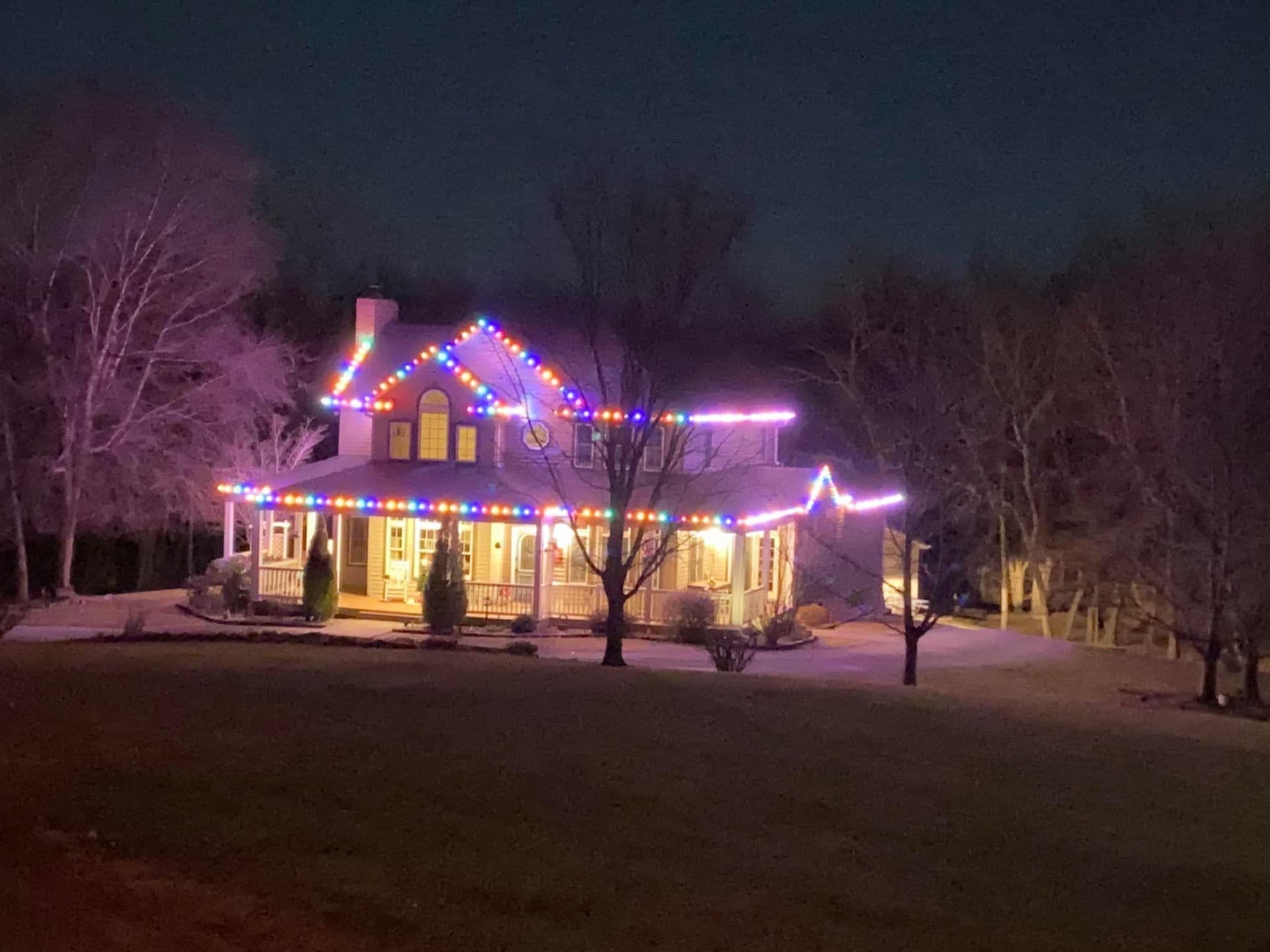 Farmhouse with multicolor Christmas lights along porch and roofline