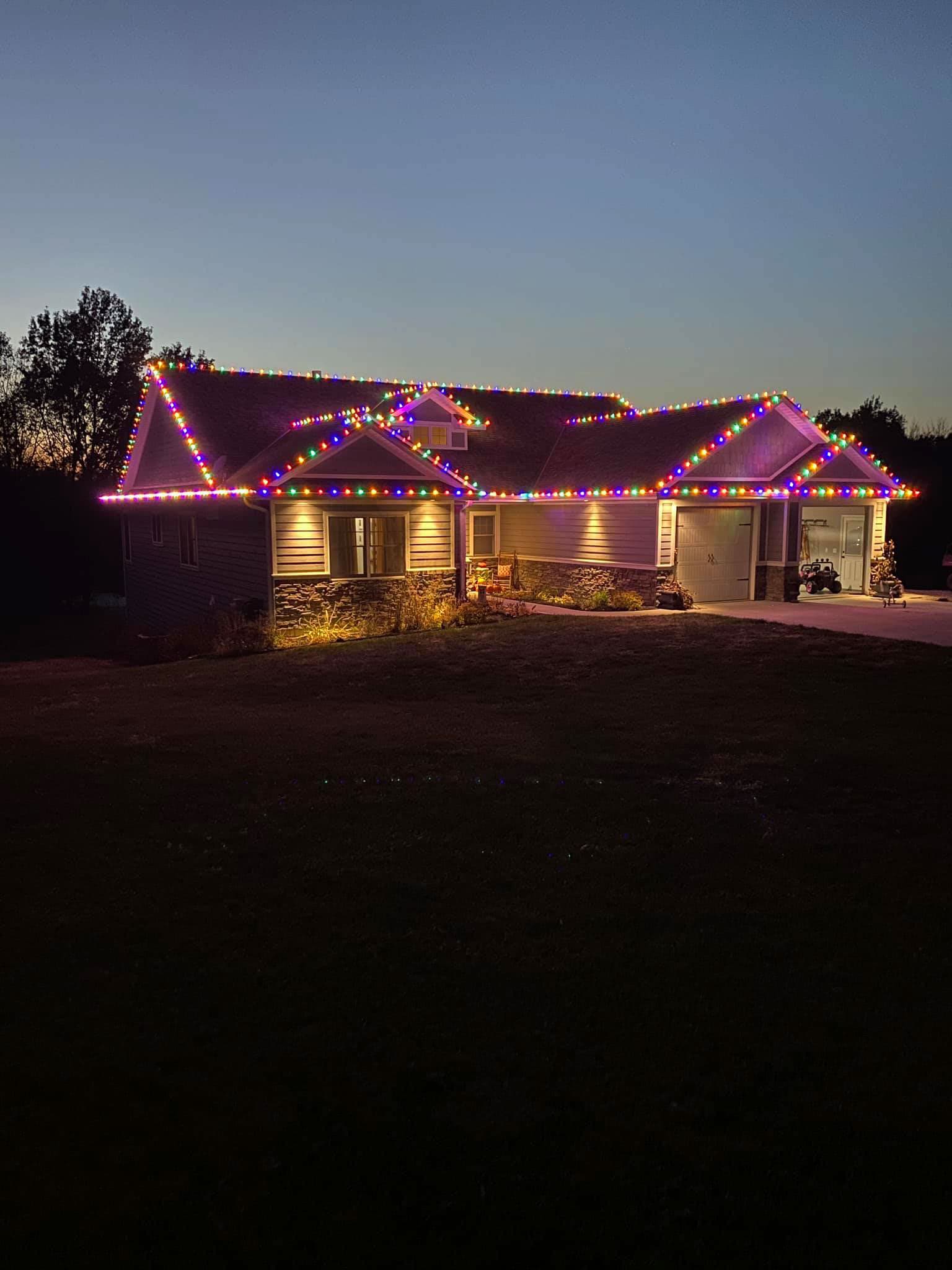 Ranch home with multicolor holiday lights on stone exterior at dusk