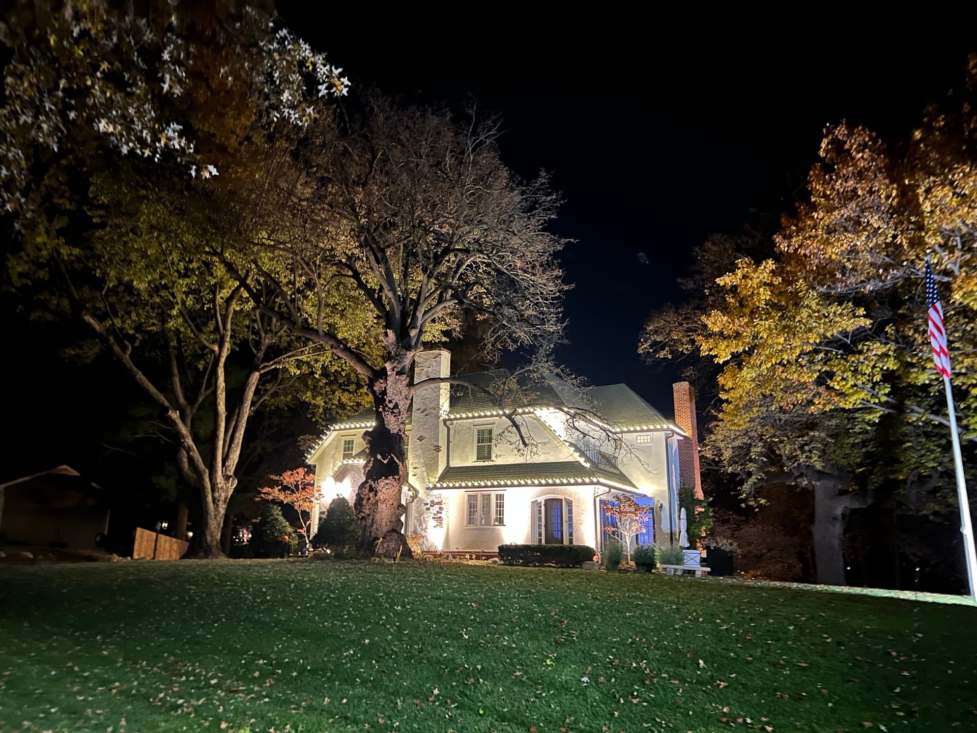 Colonial home with warm white holiday lights and American flag in Kansas City