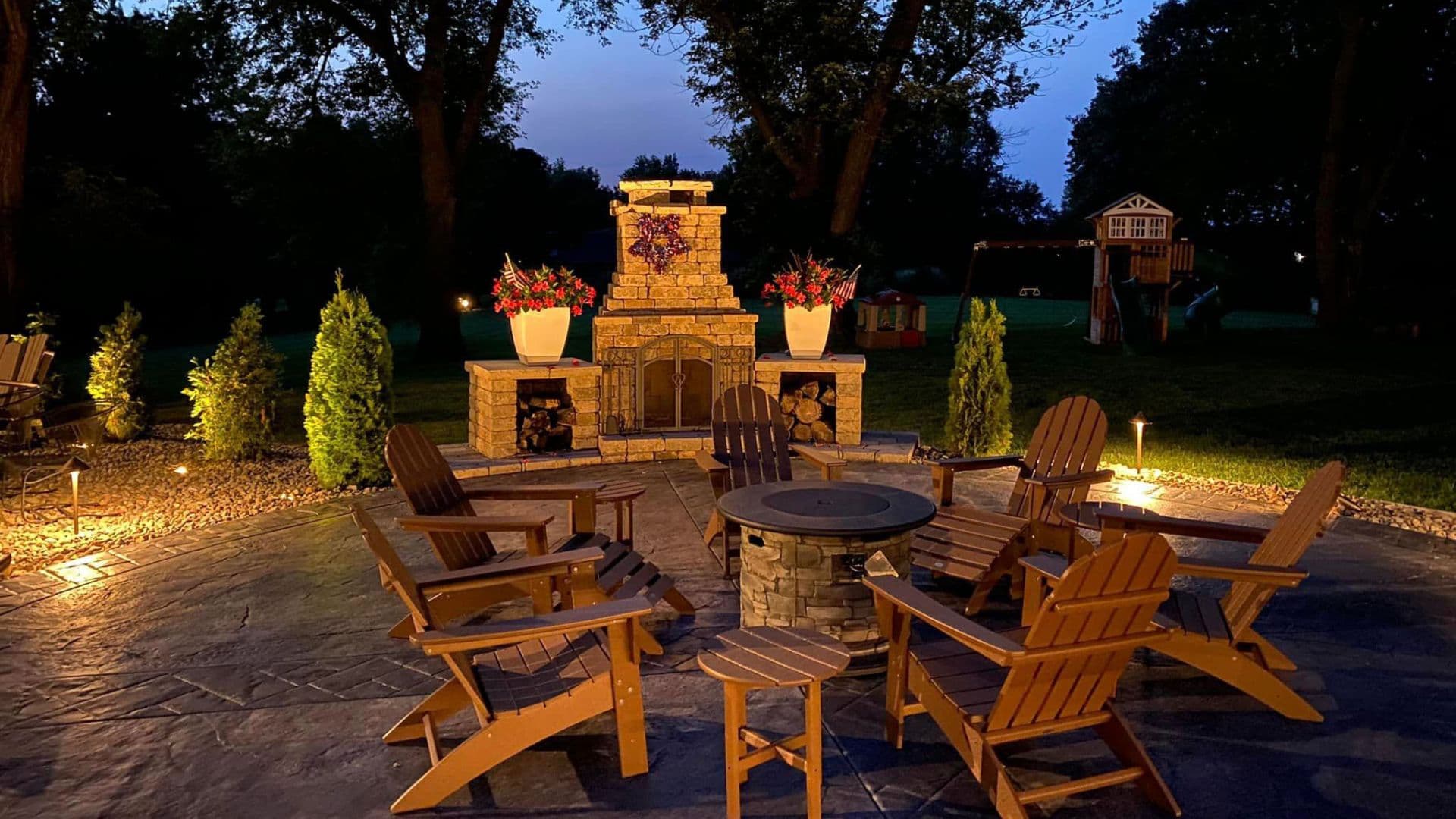 Outdoor fireplace and fire pit with patio seating illuminated at dusk