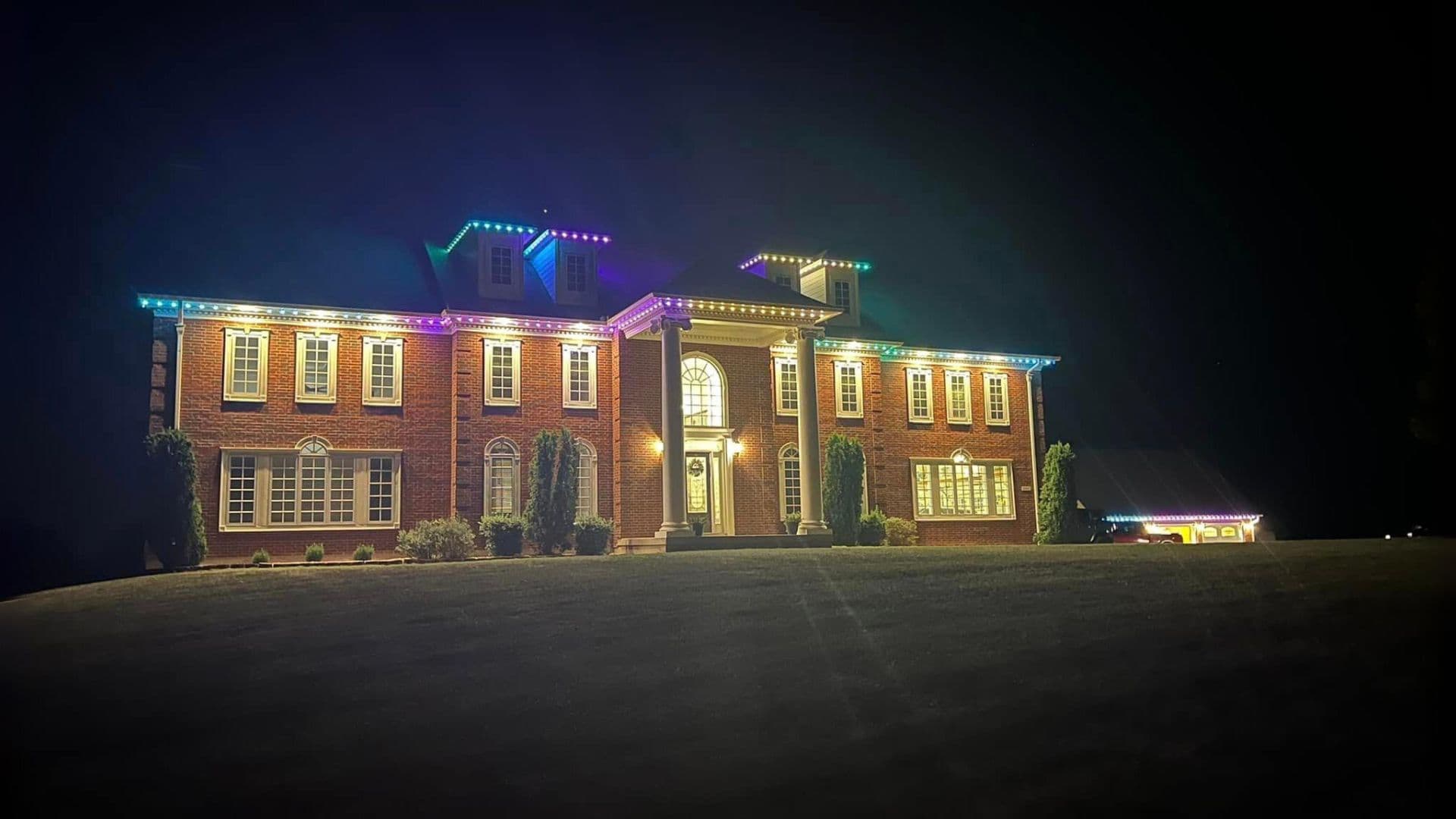 RGB permanent holiday lights on brick colonial mansion at night